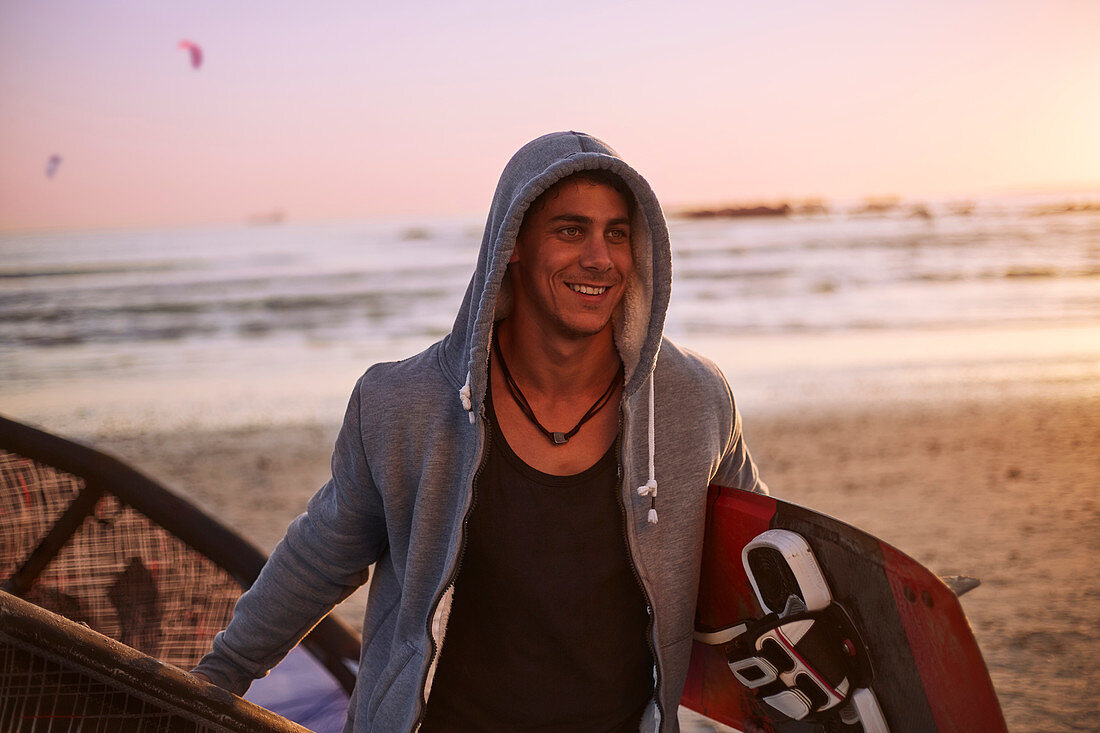 Smiling man in hoody carrying kiteboard