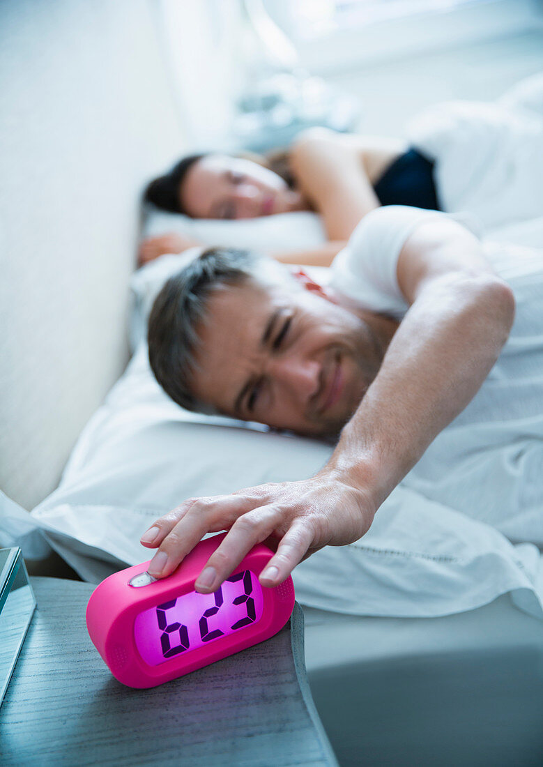 Man in bed turning off alarm clock