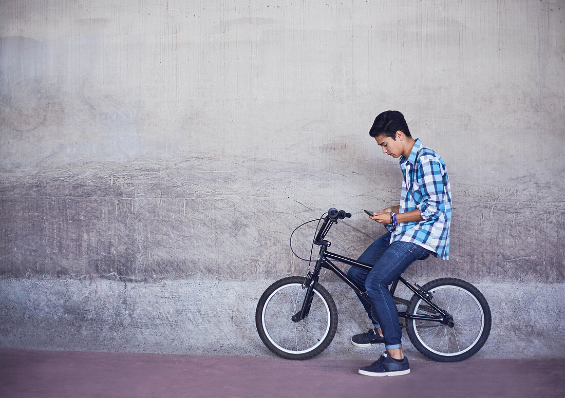 Boy texting on BMX bicycle at wall