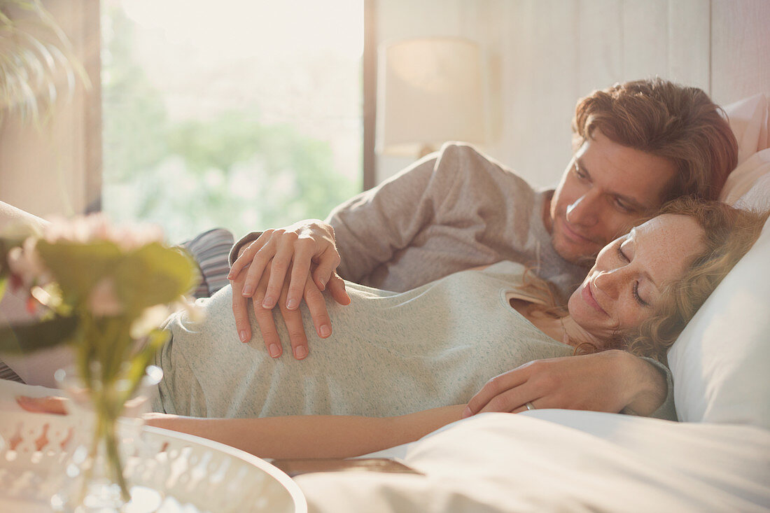 Pregnant couple holding belly on bed