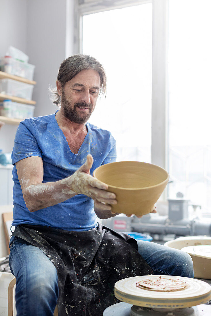 Mature man holding bowl at pottery wheel