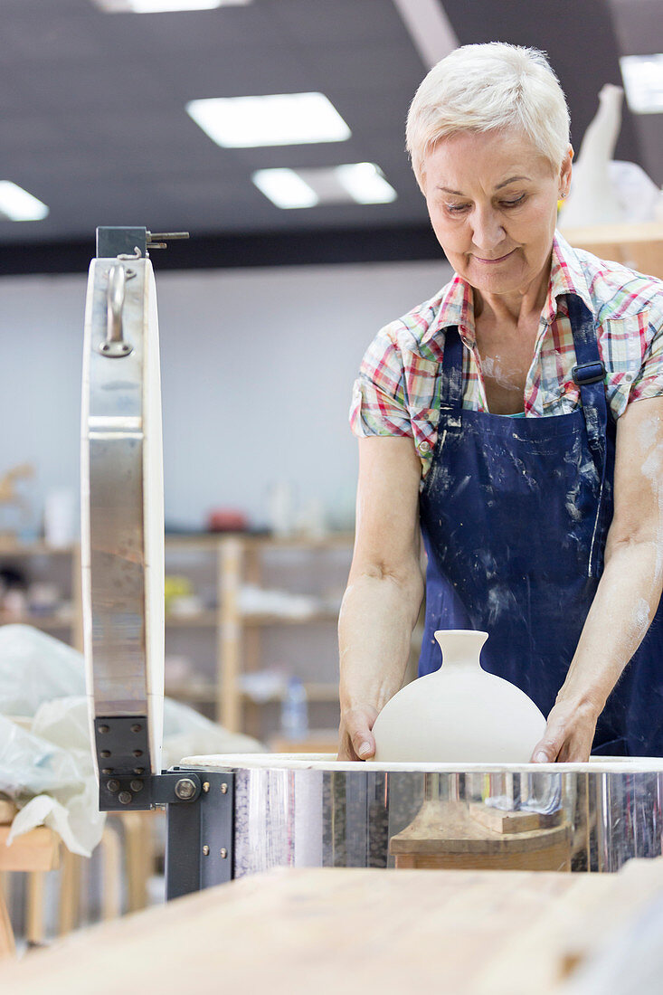 Senior woman placing pottery in kiln