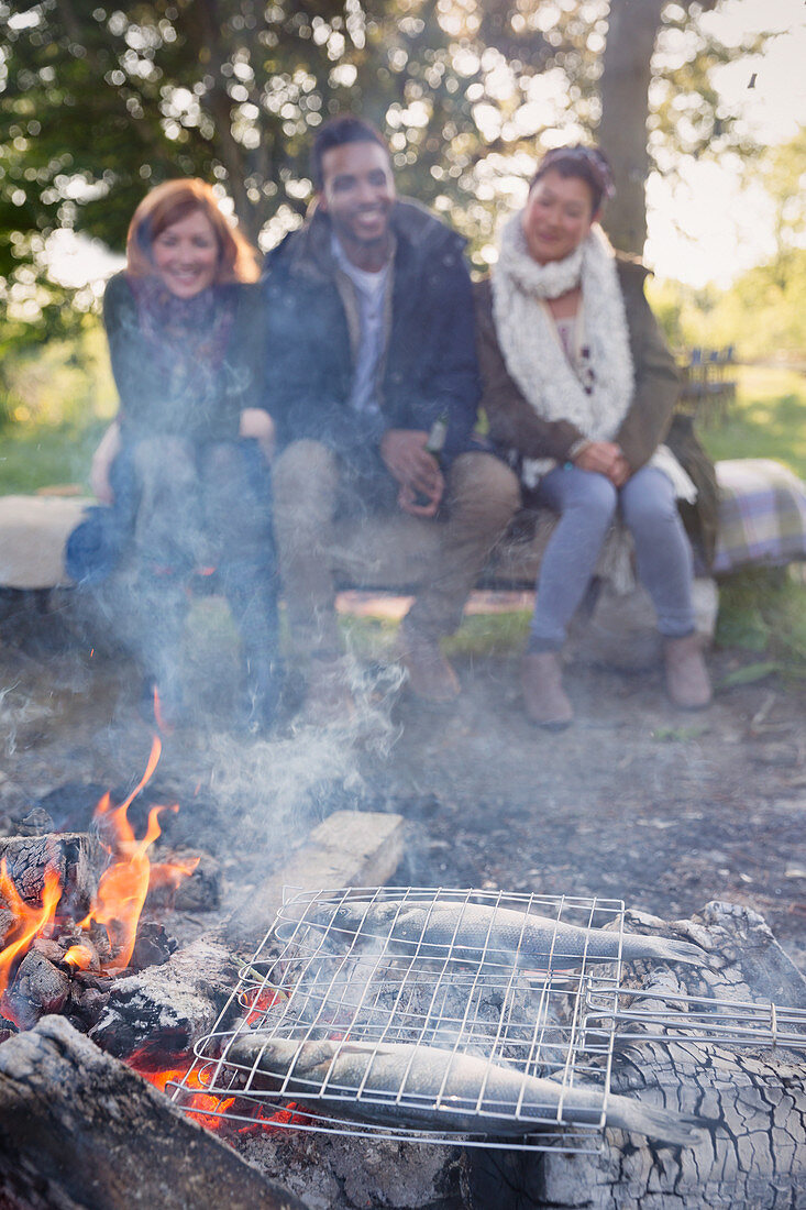 Friends watching fish cooking on campfire