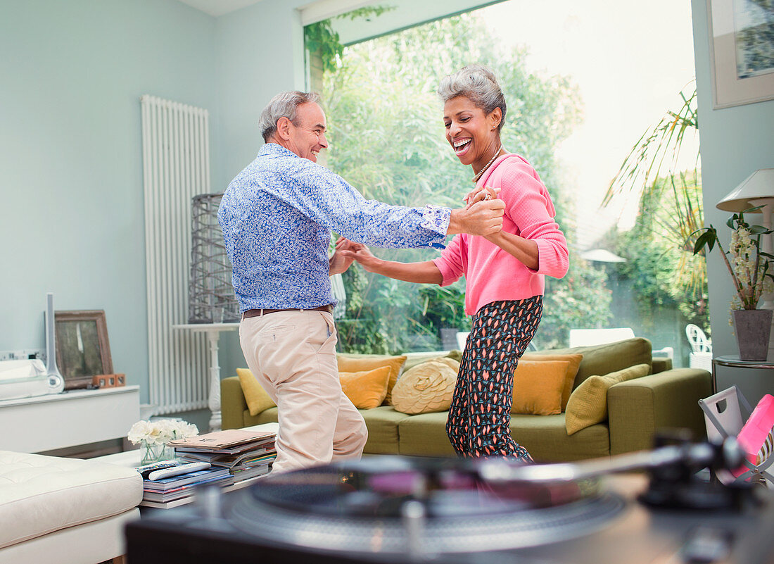 Playful mature couple dancing in living room