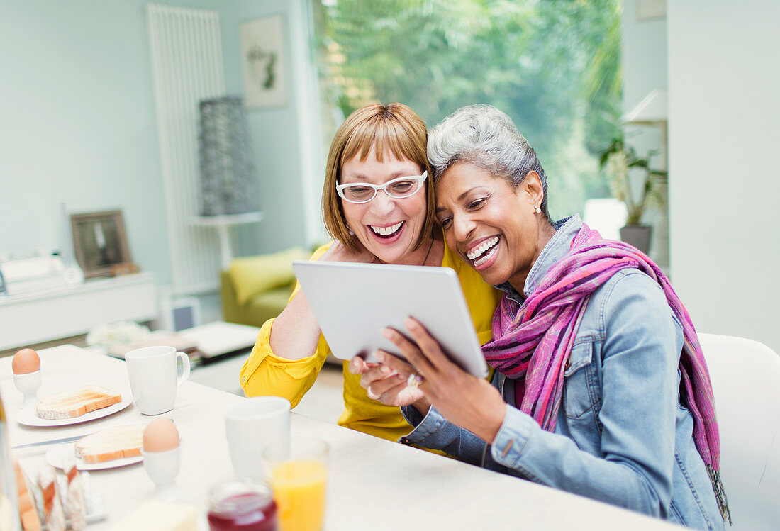 Laughing mature women sharing digital tablet