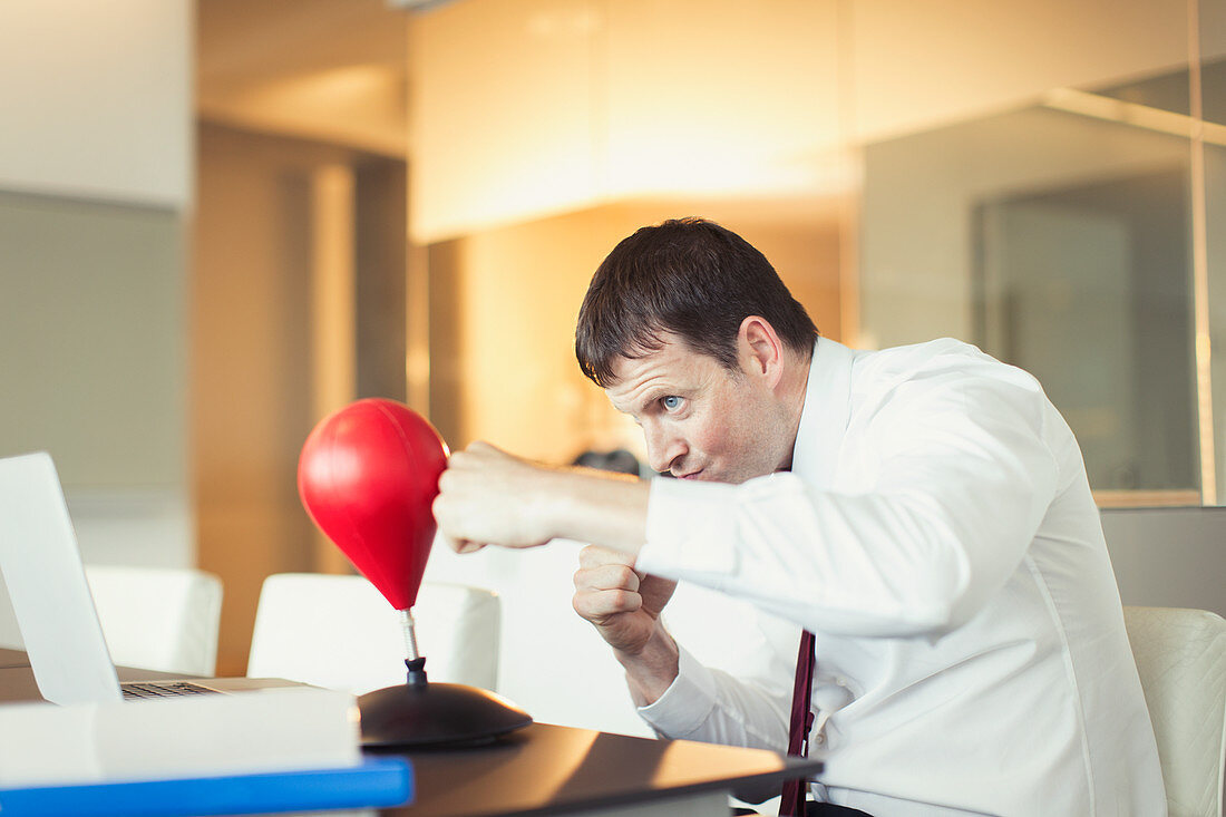 Businessman punching toy punching bag in office