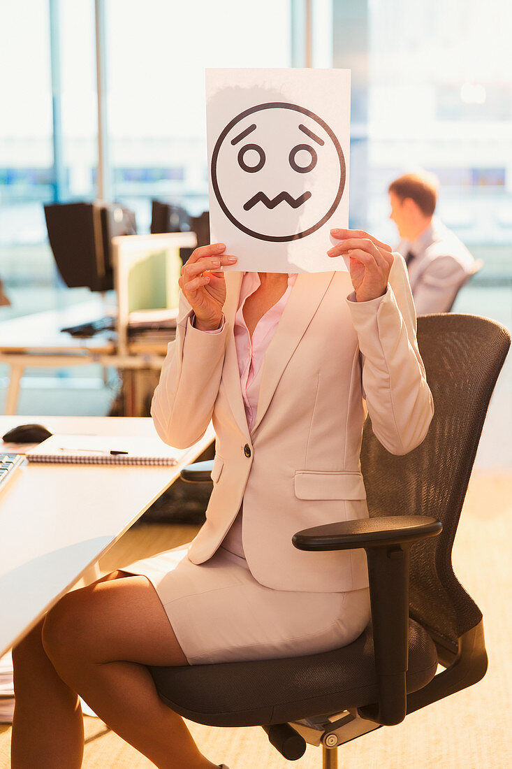 Businesswoman holding frowning face printout