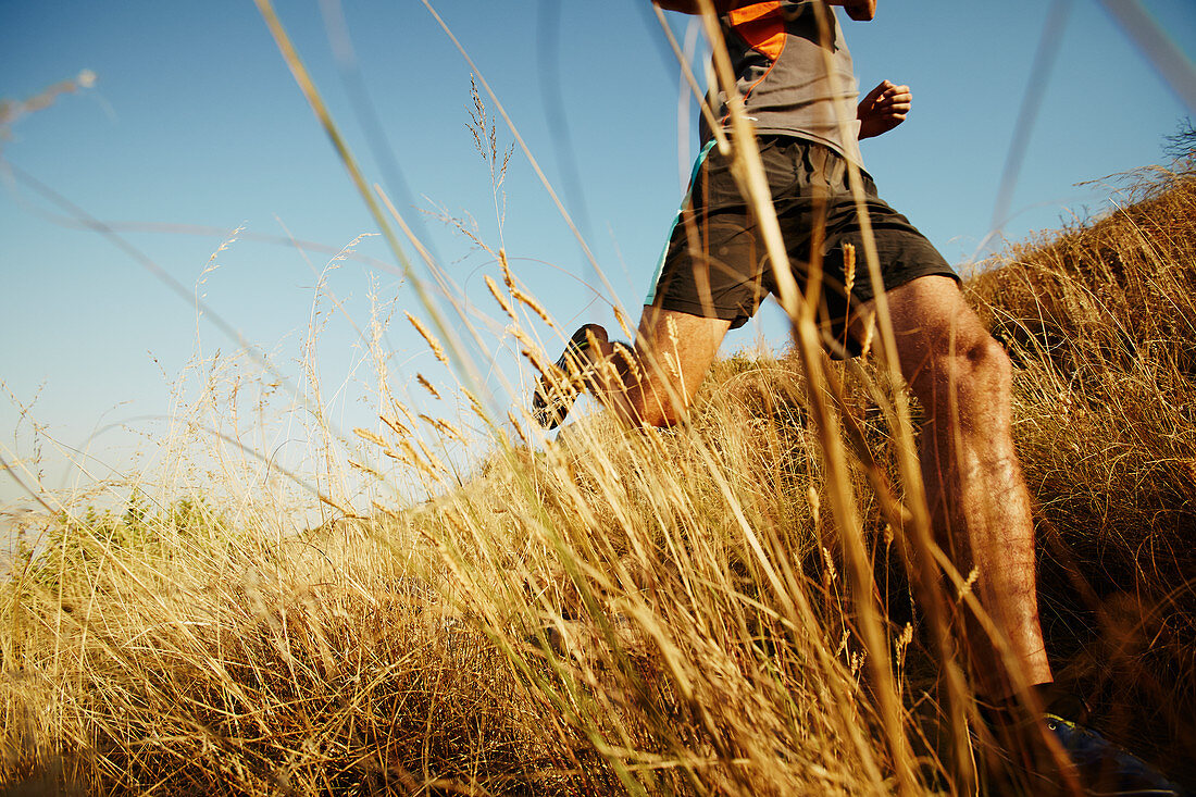 Man running through tall grass on sunny trail