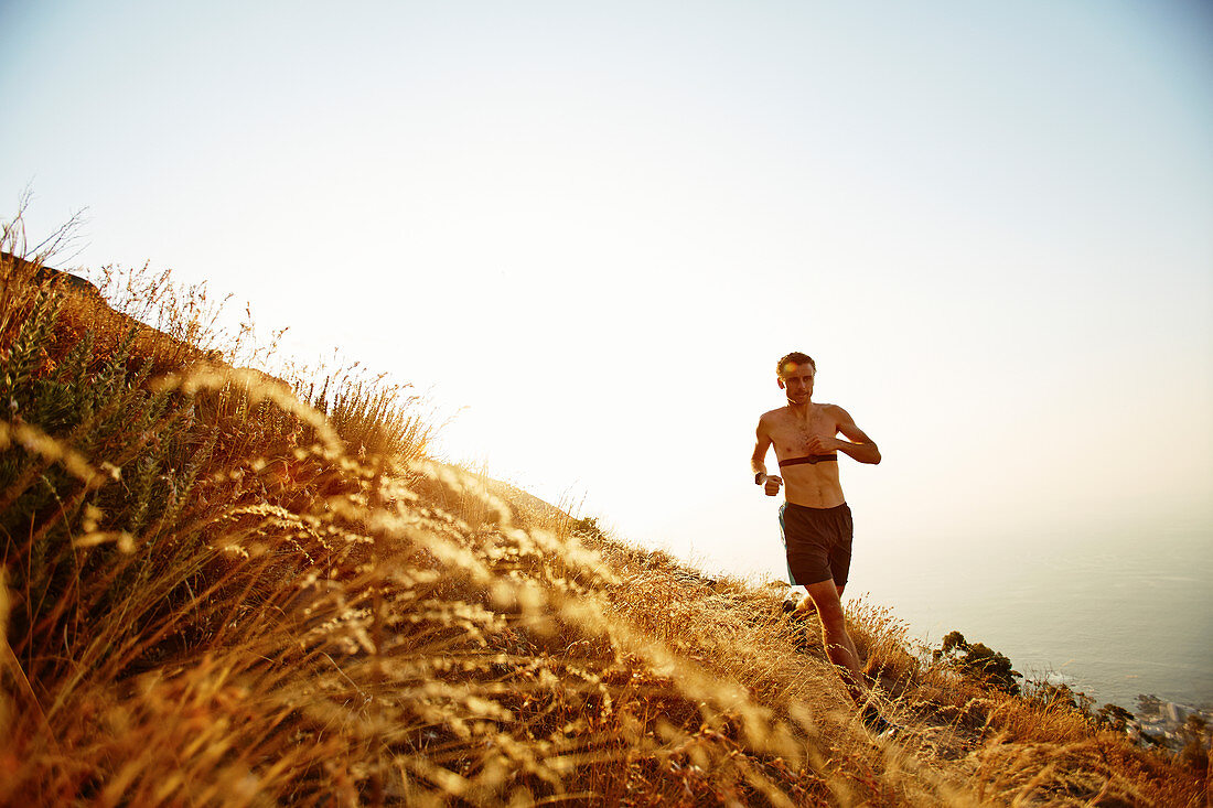 Bare chested man running on sunny hillside