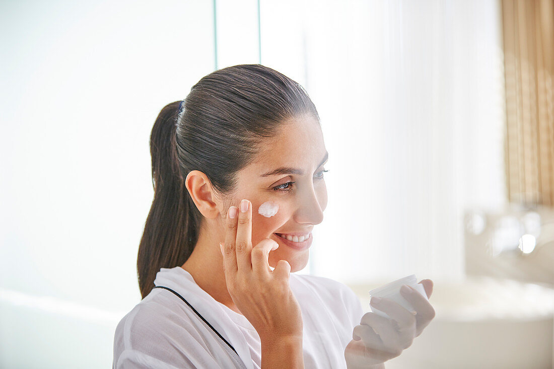 Woman applying face cream to cheek