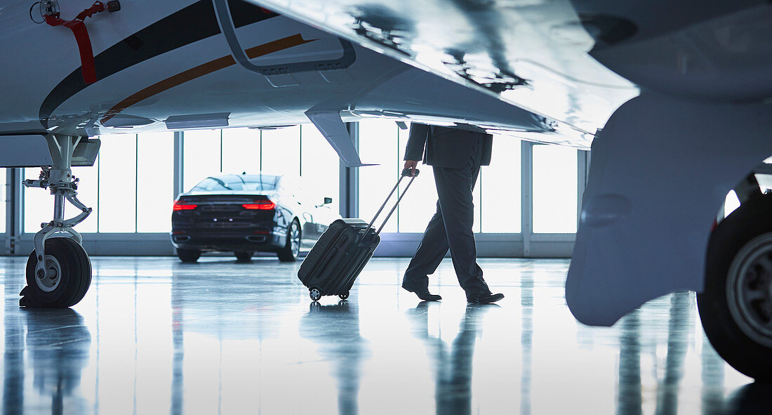 Businessman pulling suitcase outside corporate jet