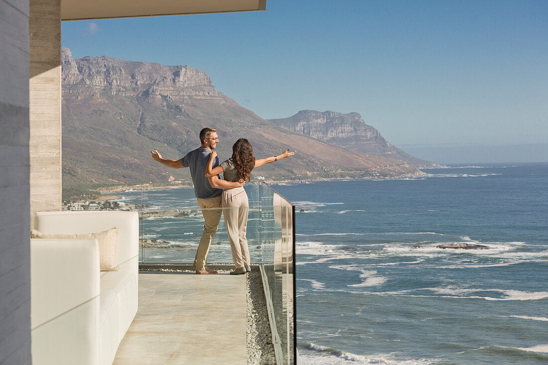 Carefree couple standing on sunny luxury balcony
