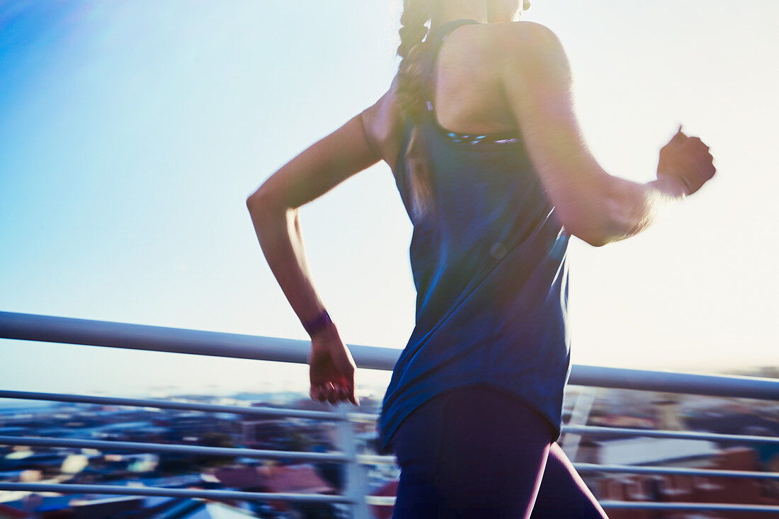 Female runner running on sunny urban footbridge