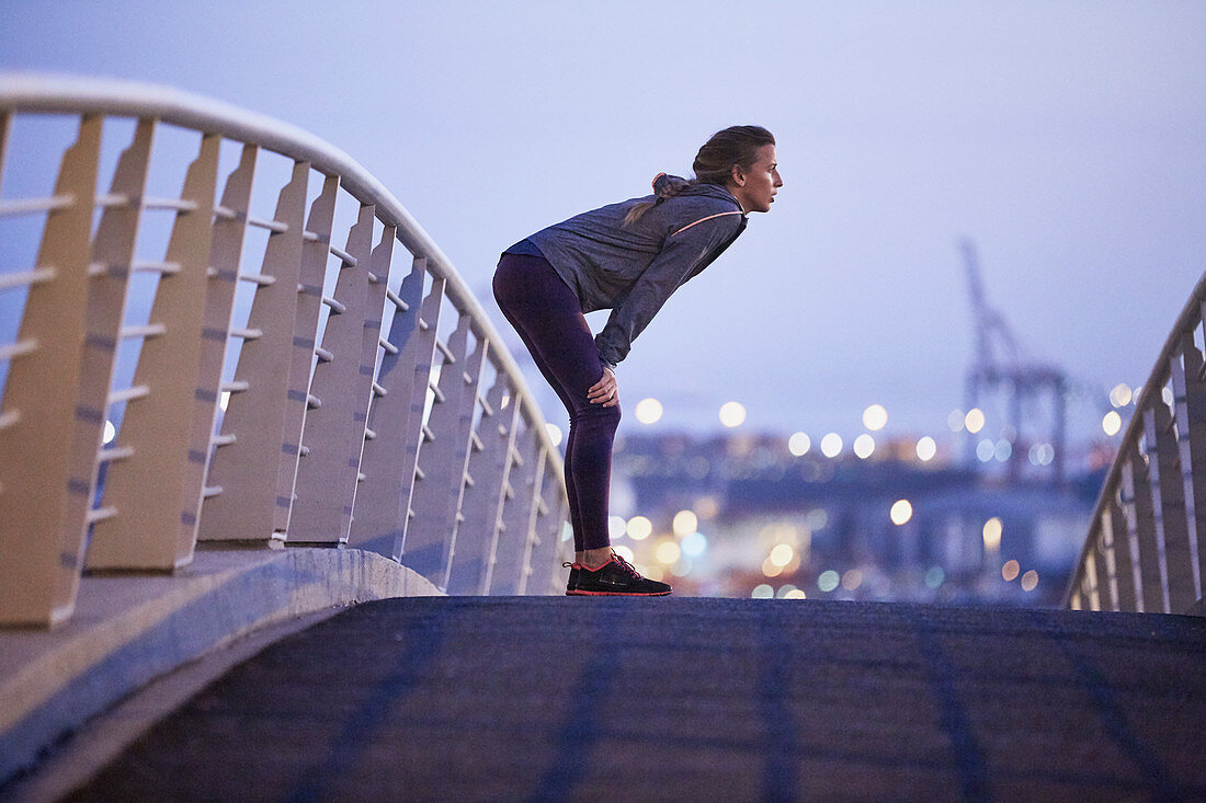 Female runner resting on urban footbridge at dawn