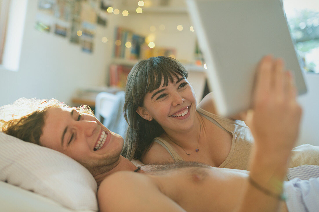 Smiling young couple using digital tablet in bed