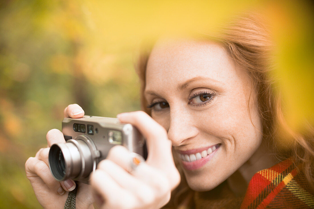 Woman using digital camera among autumn leaves
