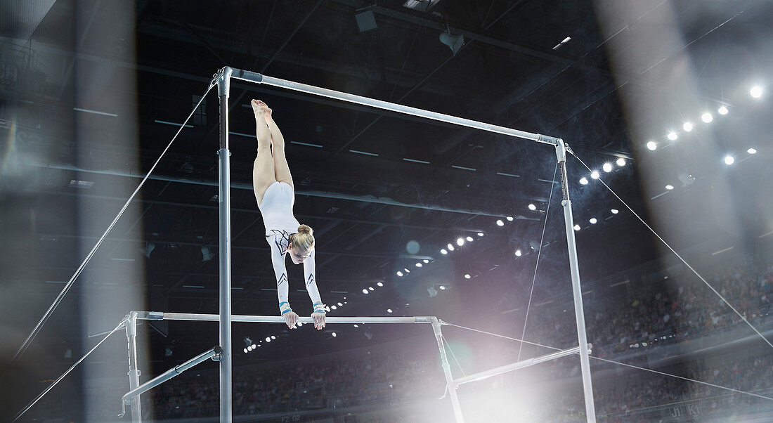 Female gymnast performing on uneven bars in arena