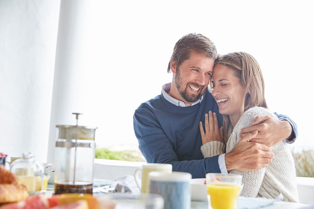 Smiling couple hugging at patio breakfast table