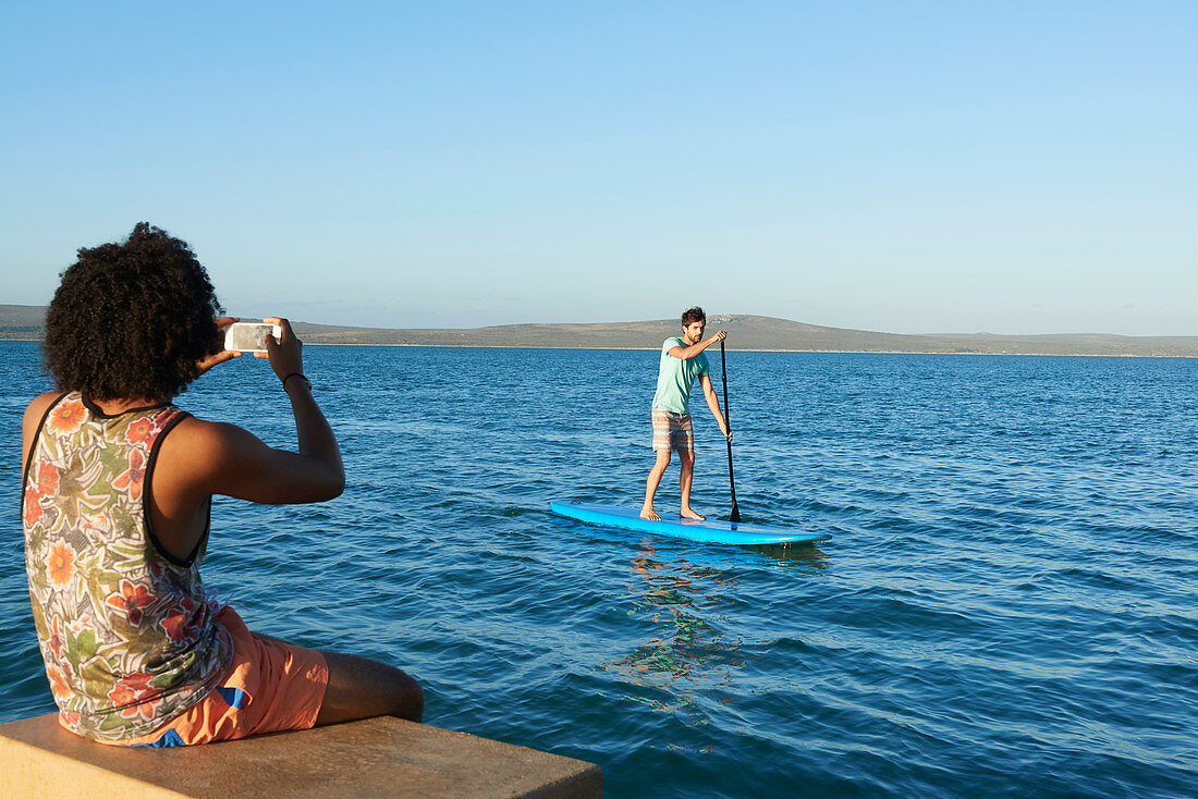 Young man photographing friend paddleboarding