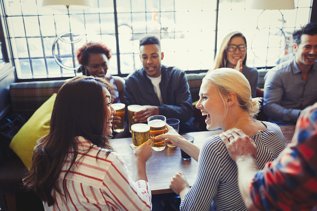 Laughing friends toasting beer glasses in bar