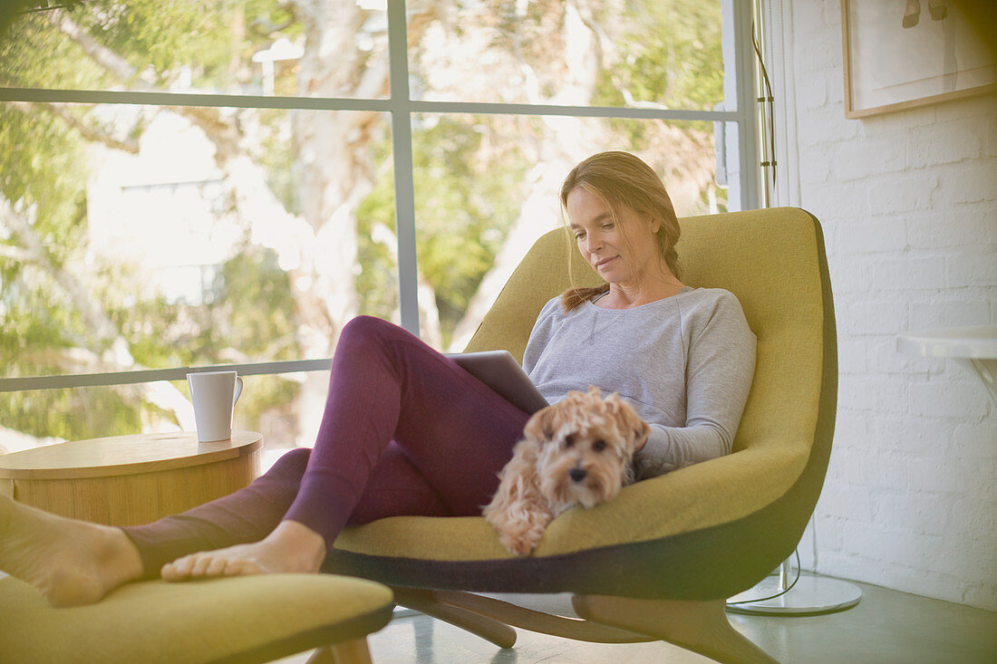 Woman with dog using digital tablet in chair
