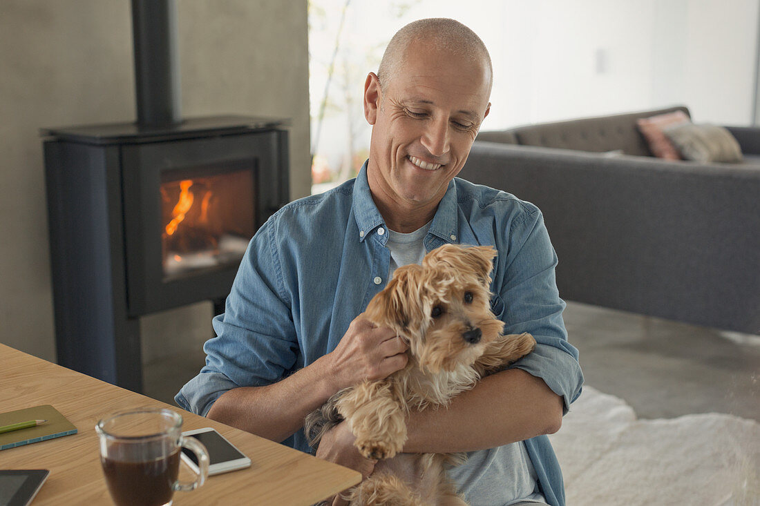 Smiling man petting dog in front of fireplace