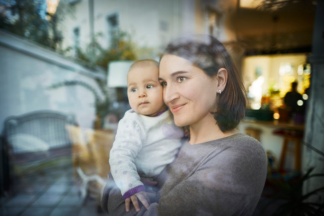 Smiling mother holding baby daughter at window