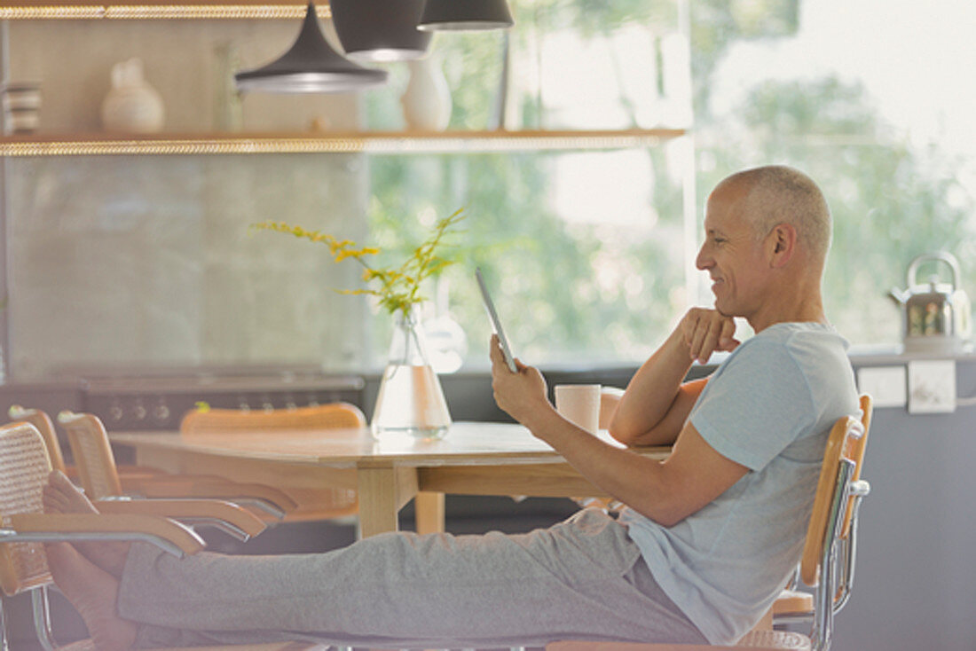 Mature man relaxing, using tablet with feet up