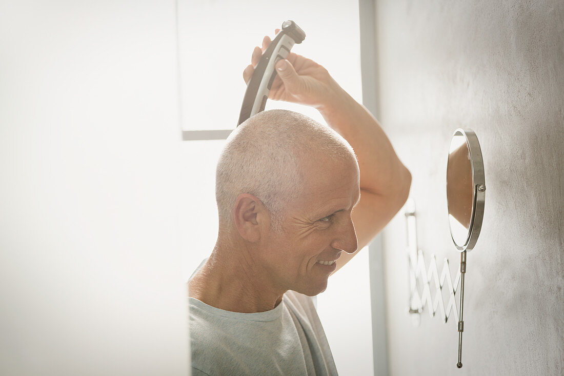 Mature man shaving head with electric razor