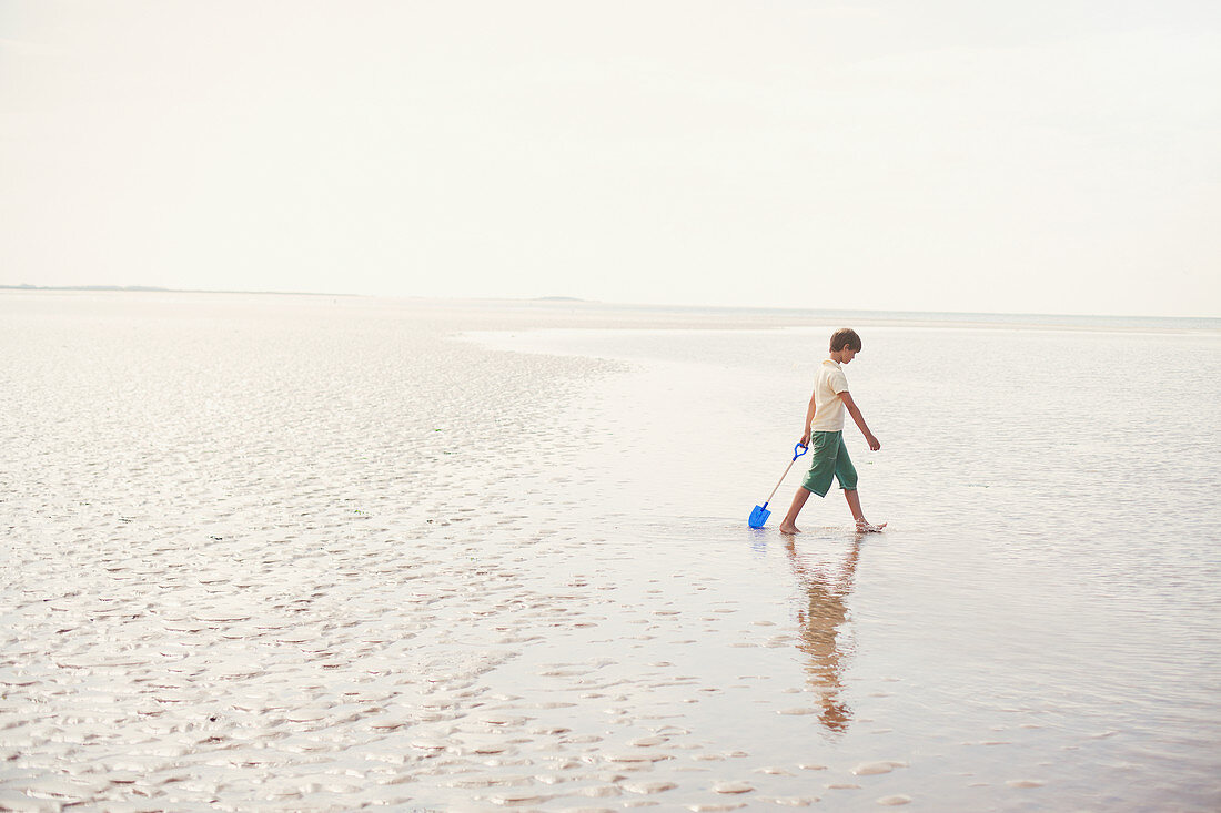 Boy walking with shovel in wet sand