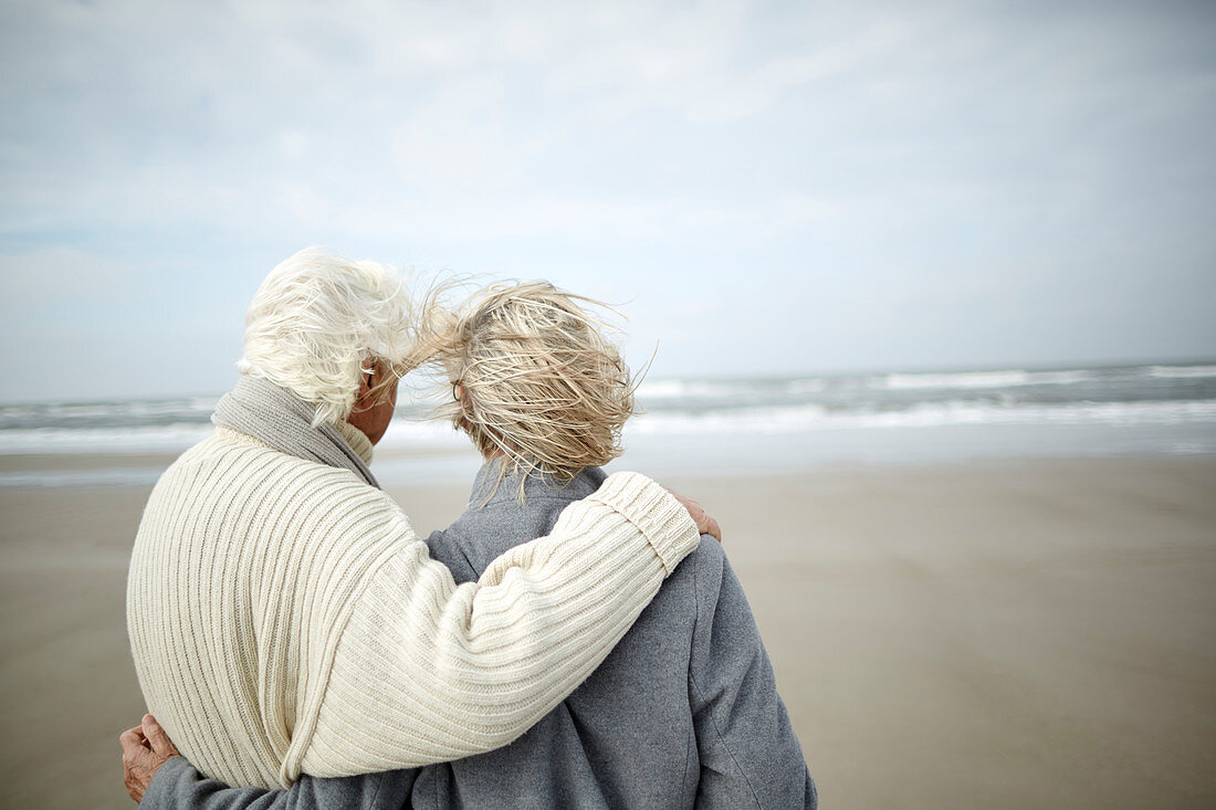 Pensive senior couple hugging on beach