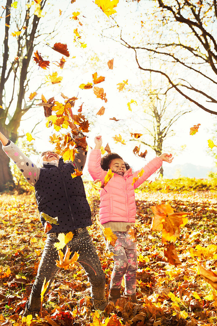 Playful sisters throwing autumn leaves