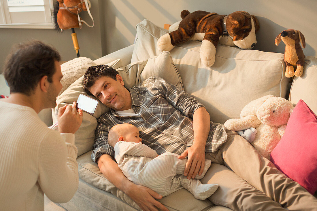 Male gay parents and baby son resting on sofa