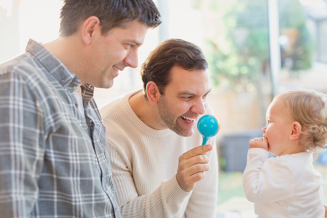 Male gay parents and baby son playing with rattle