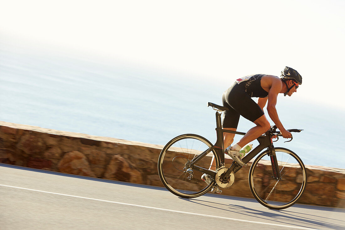 Male triathlete cyclist racing on ocean road