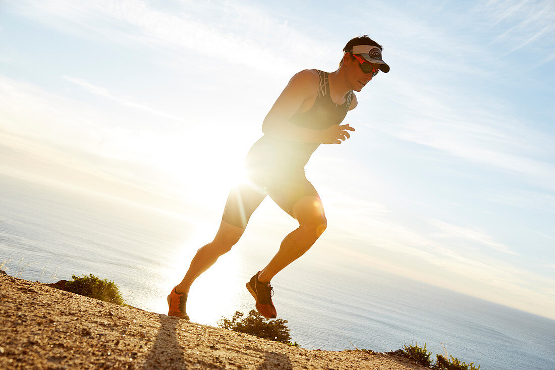 Male triathlete runner running along ocean