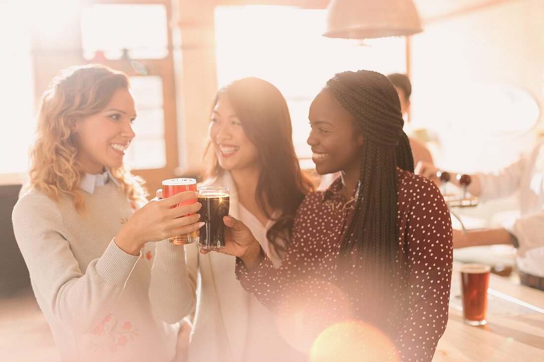 Women friends toasting beer glasses at bar