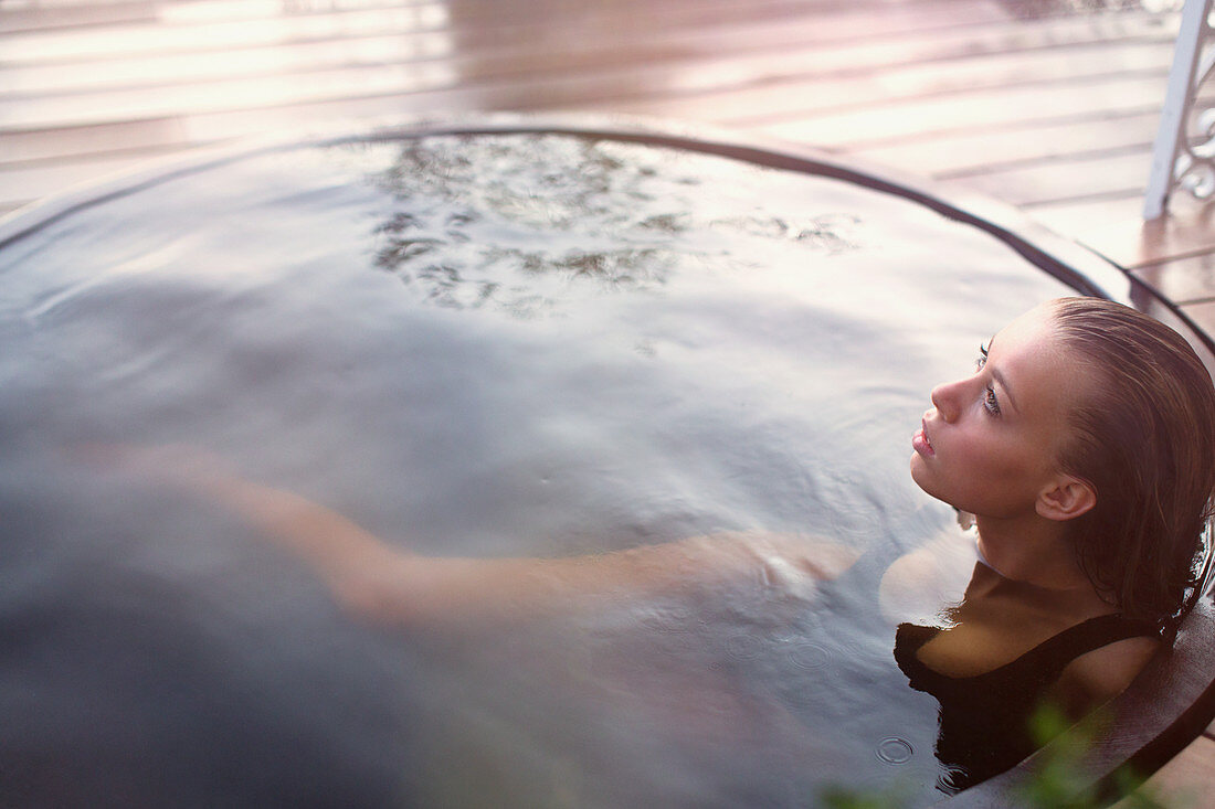 Serene teenage girl soaking in hot tub on patio