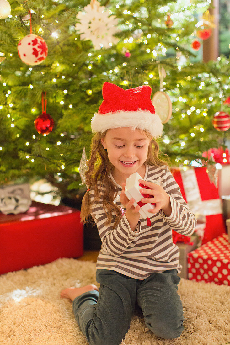 Smiling girl in Santa hat opening gift