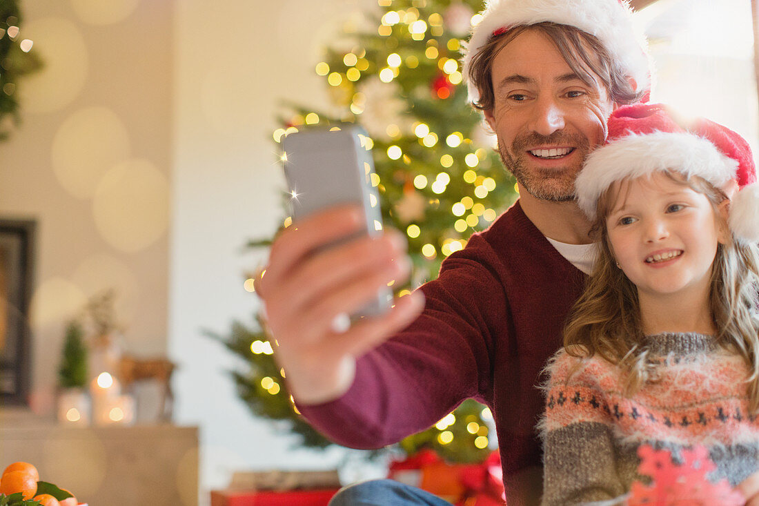Father and daughter in Santa hats taking selfie