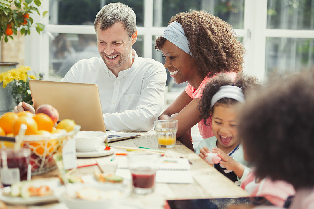 Young family using laptop and eating breakfast