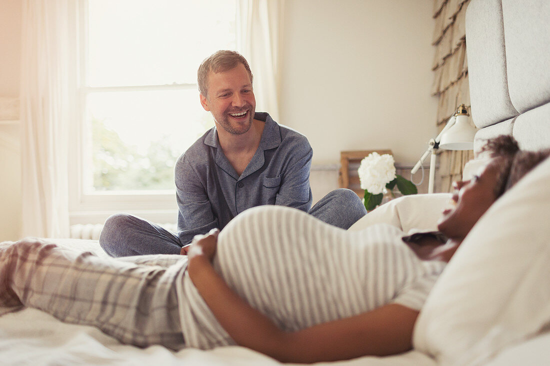 Multi-ethnic pregnant couple relaxing and on bed