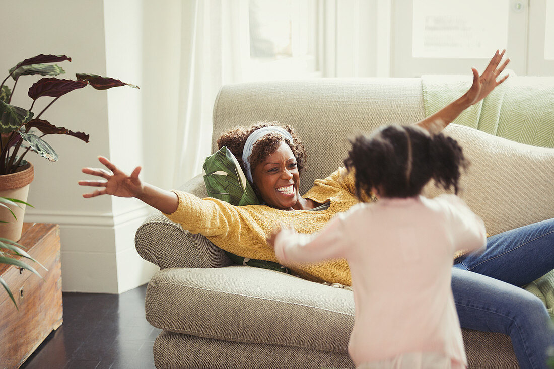 Mother on sofa greeting running daughter