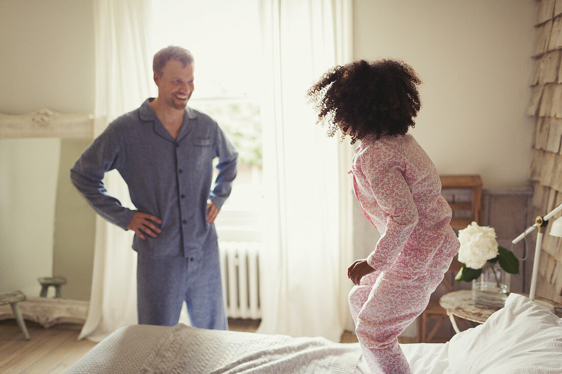 Father in pyjamas watching daughter jumping on bed