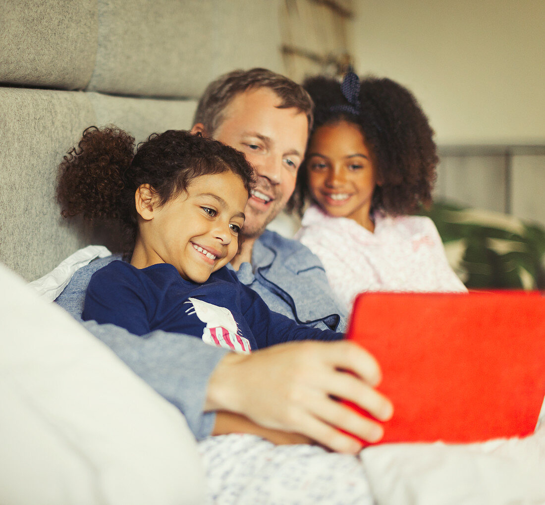 Multi-ethnic father and daughters on bed