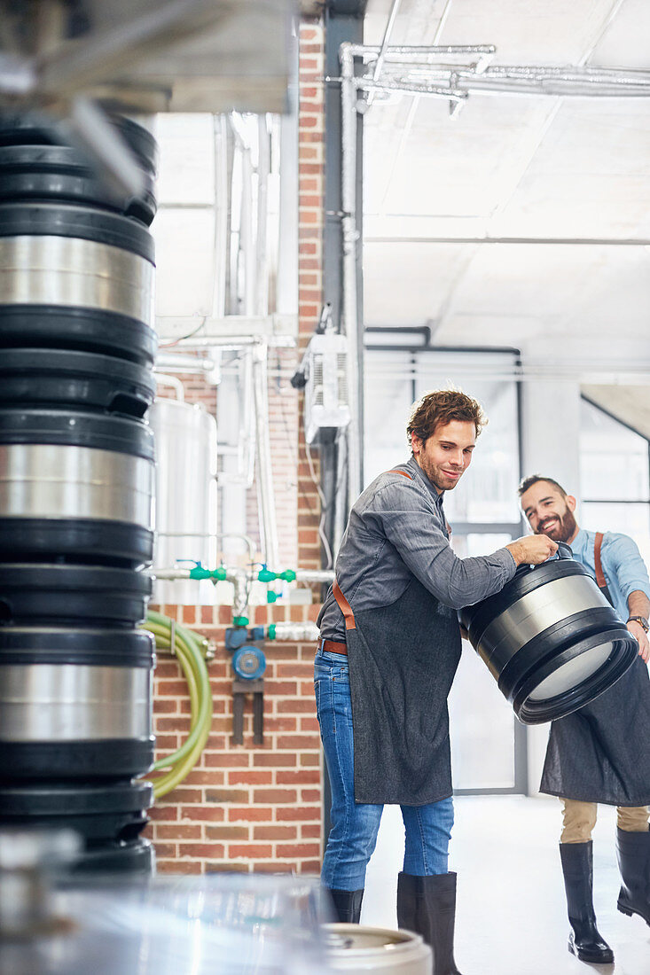 Male brewers carrying kegs in brewery