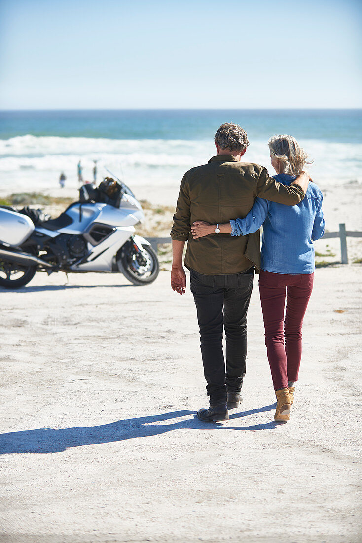 Senior couple walking on beach toward motorcycle