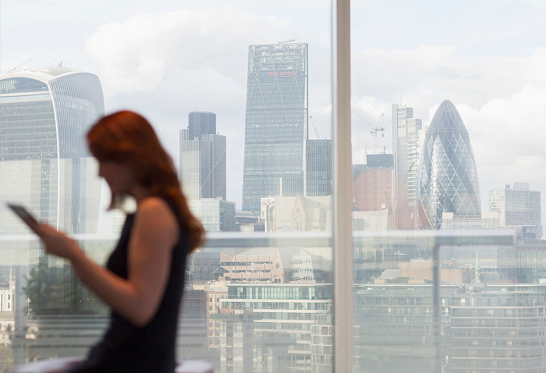 Businesswoman at window with city view, London, UK