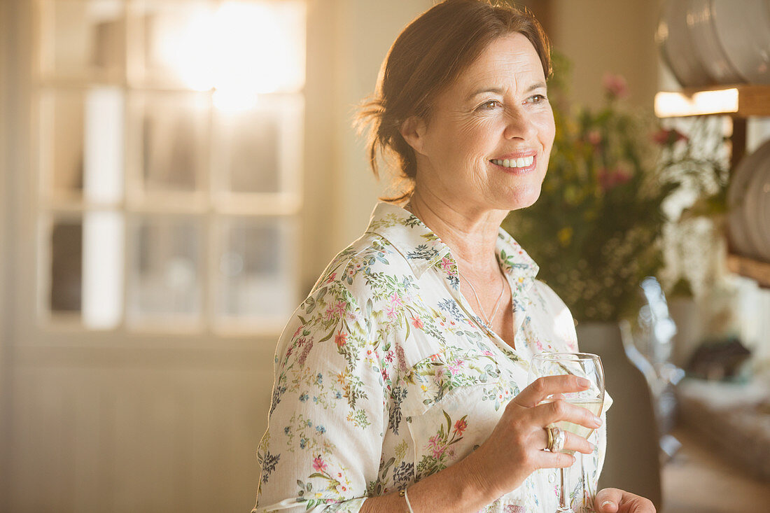 Smiling mature woman drinking wine in kitchen