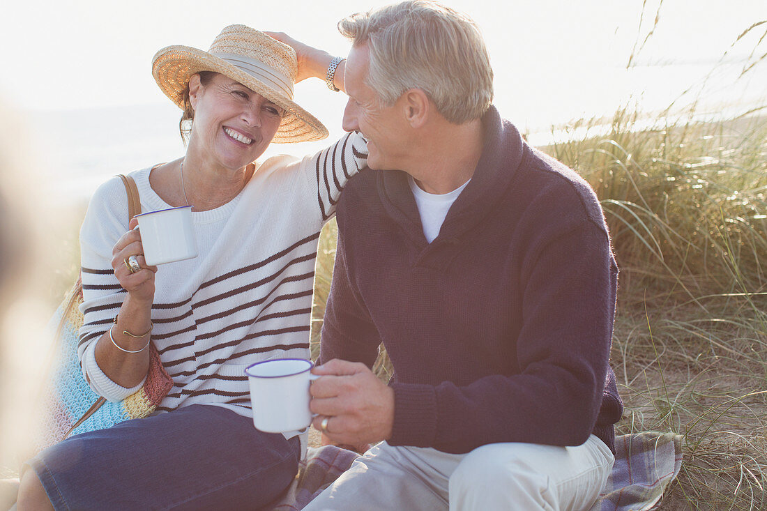 Mature couple drinking coffee in sunny beach grass